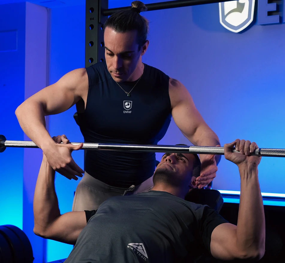 Entrenador supervisando el entrenamiento de fuerza de una alumna en el gimnasio